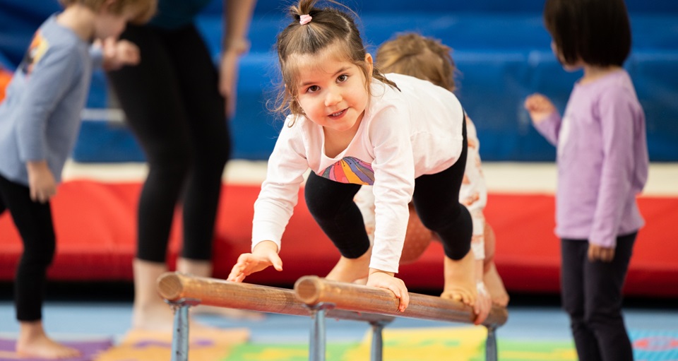 Young girl climbing along parallel bars at kids gymnastics
