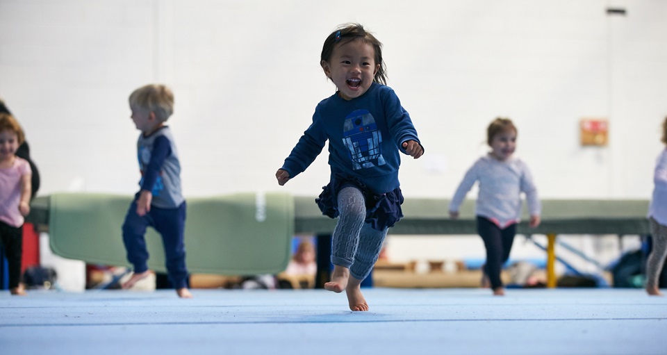 Happy young girl running on floor mat at kids gymnastics